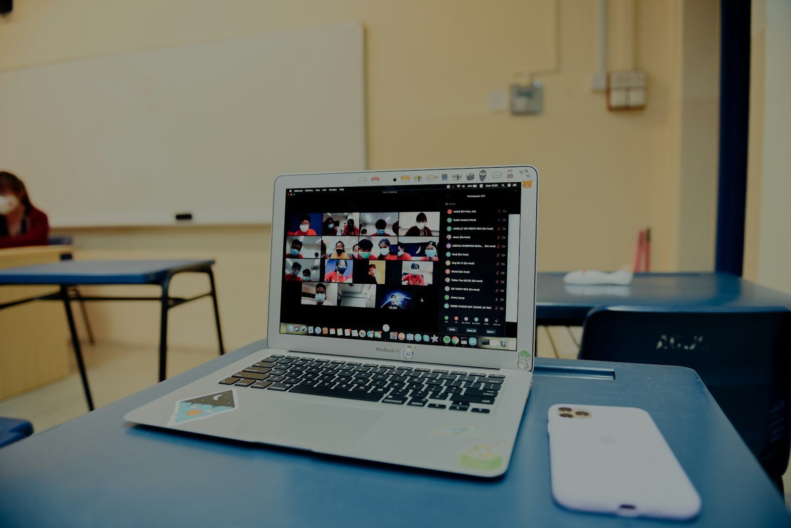 Laptop sobre un pupitre escolar mostrando una videollamada en cuadrícula durante una clase virtual