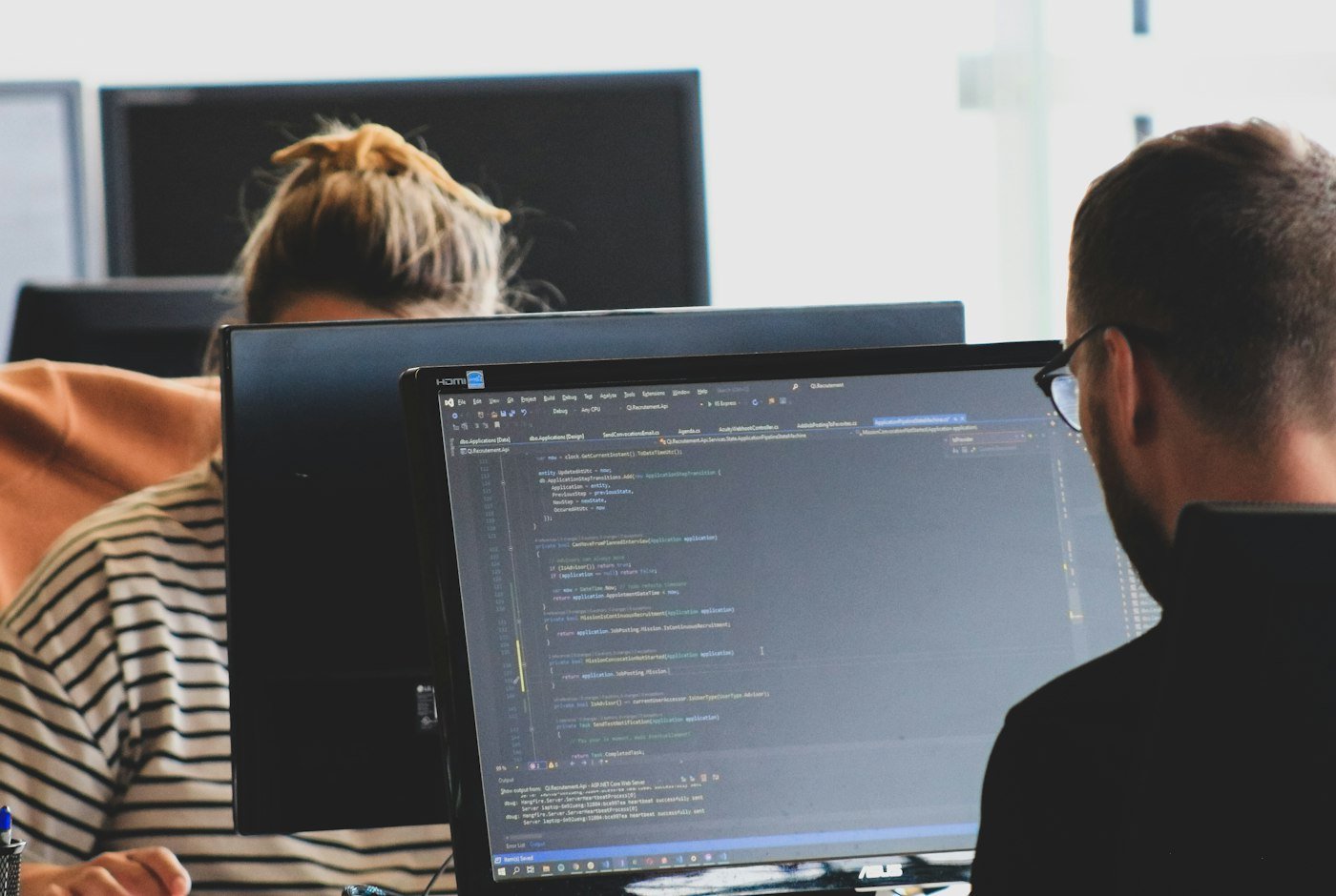 Dos profesionales de software revisando código en una estación de trabajo con varias pantallas